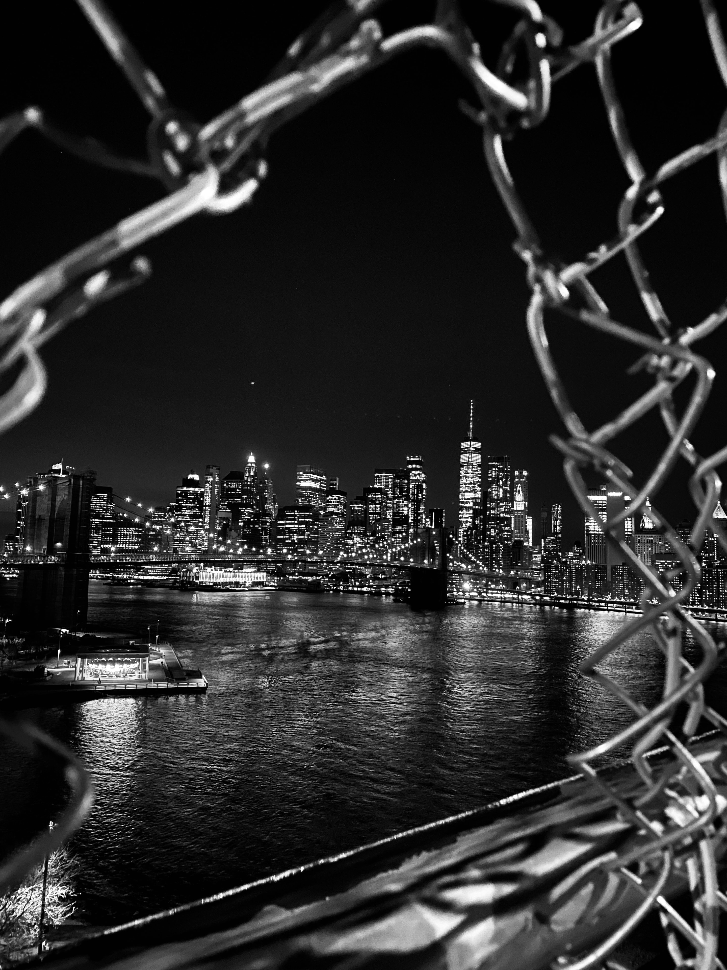 New York City skyline viewed through chain-link fence in black and white