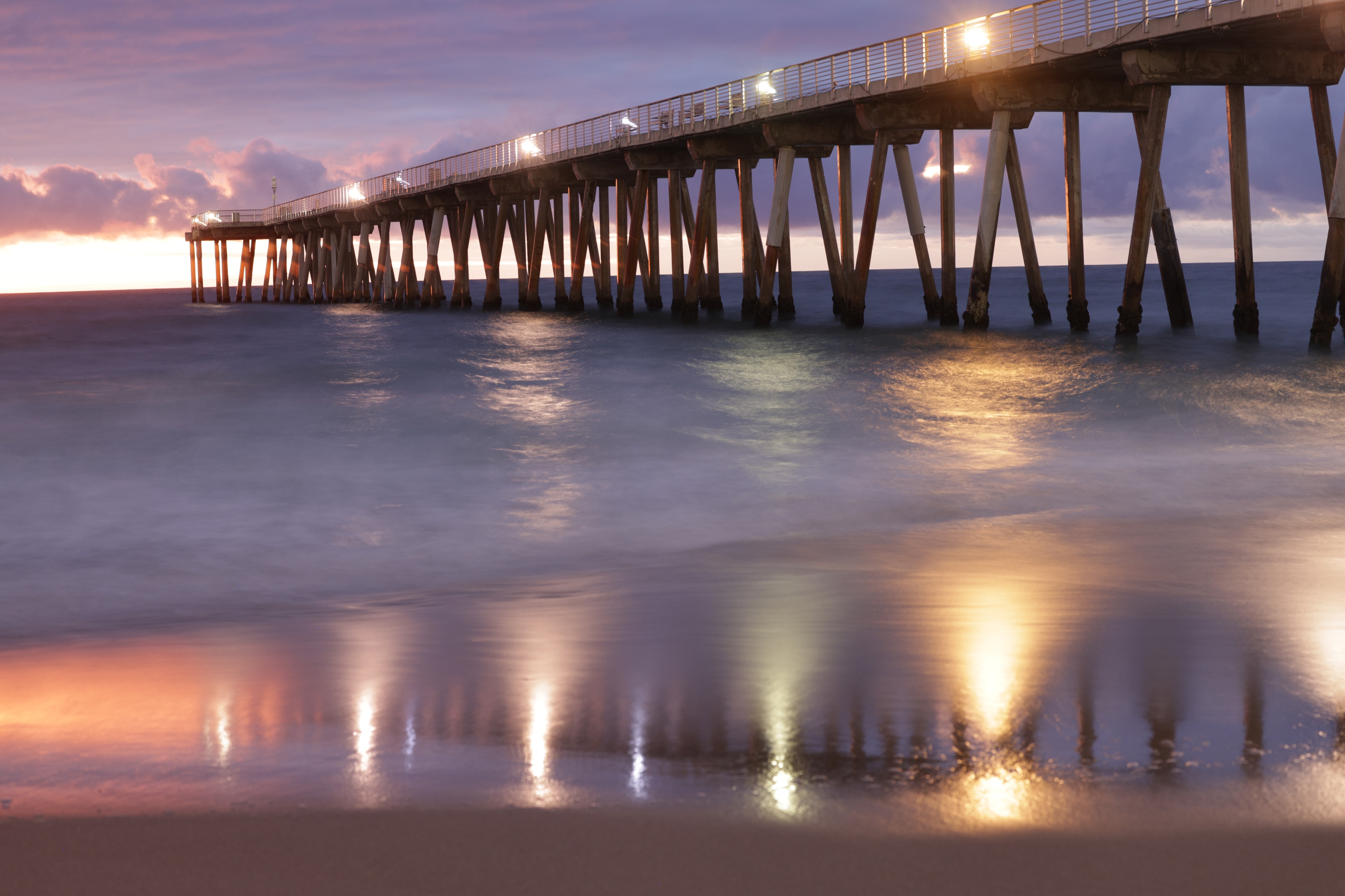 Pier at dusk with warm golden lights reflecting on silky long-exposure water