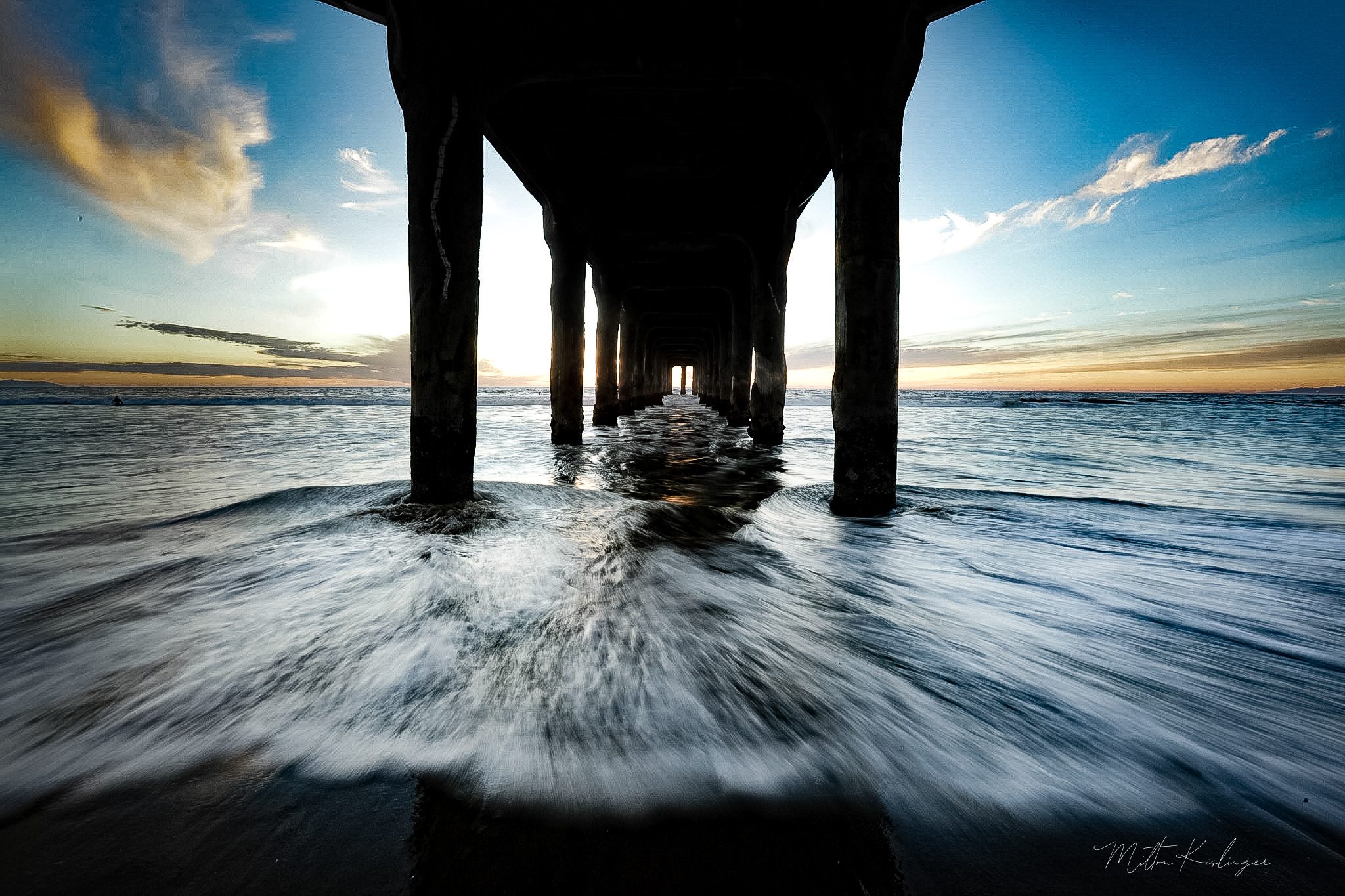 Under the pier at sunset with crashing waves and dramatic blue sky tunnel perspective