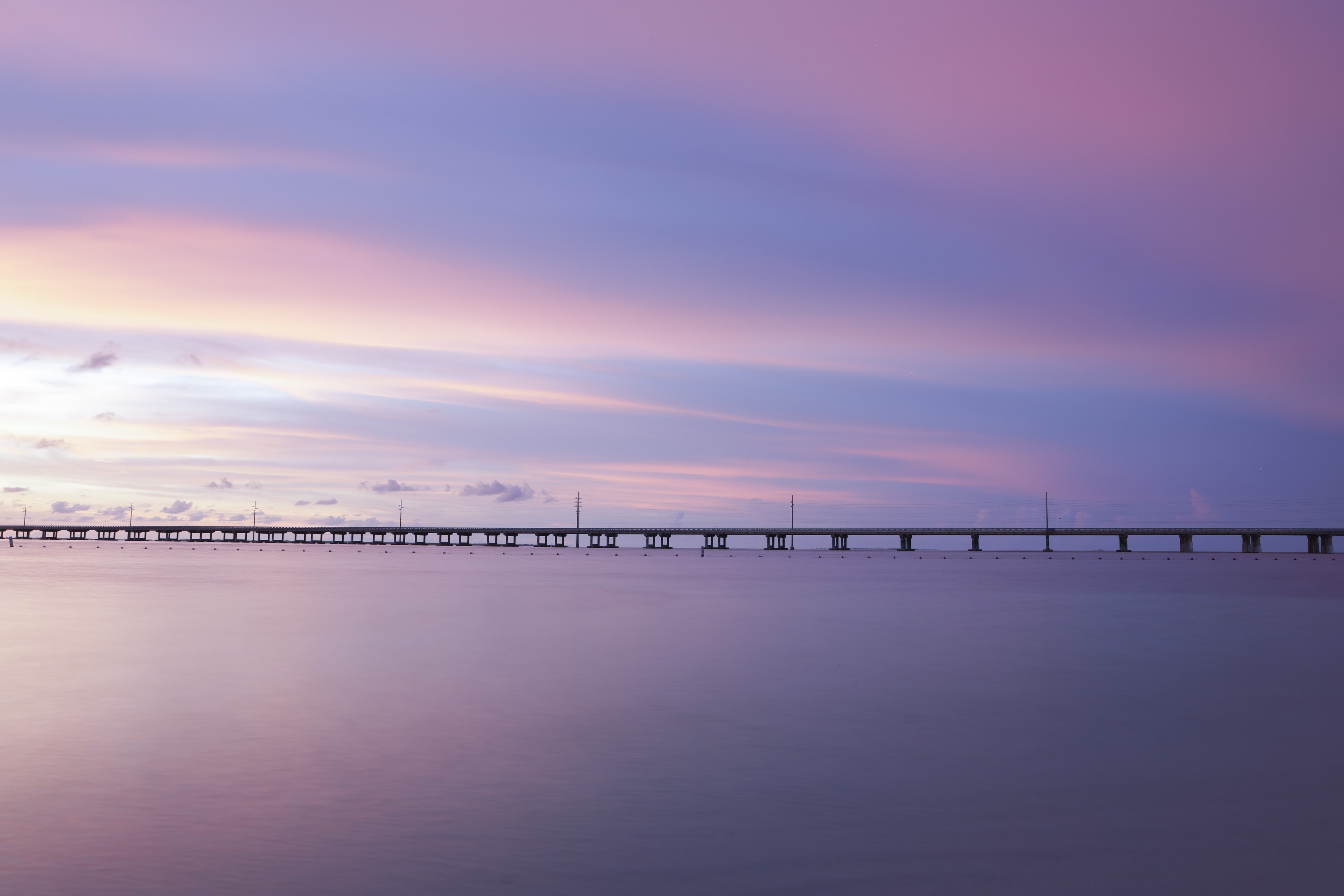 Long bridge stretching across turquoise water under a pastel purple and pink sunset sky