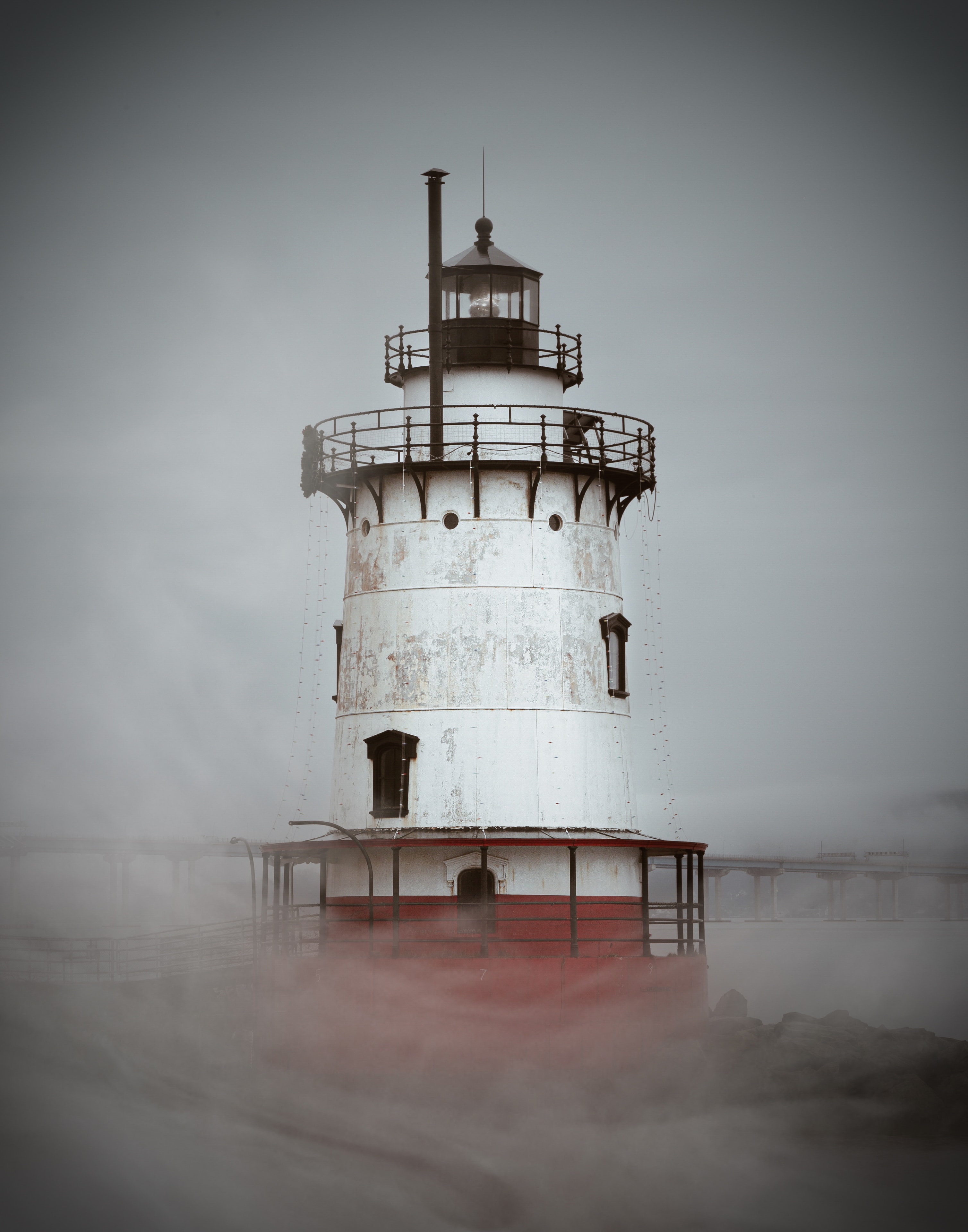 Foggy lighthouse with rust-red and white tower emerging through atmospheric coastal mist