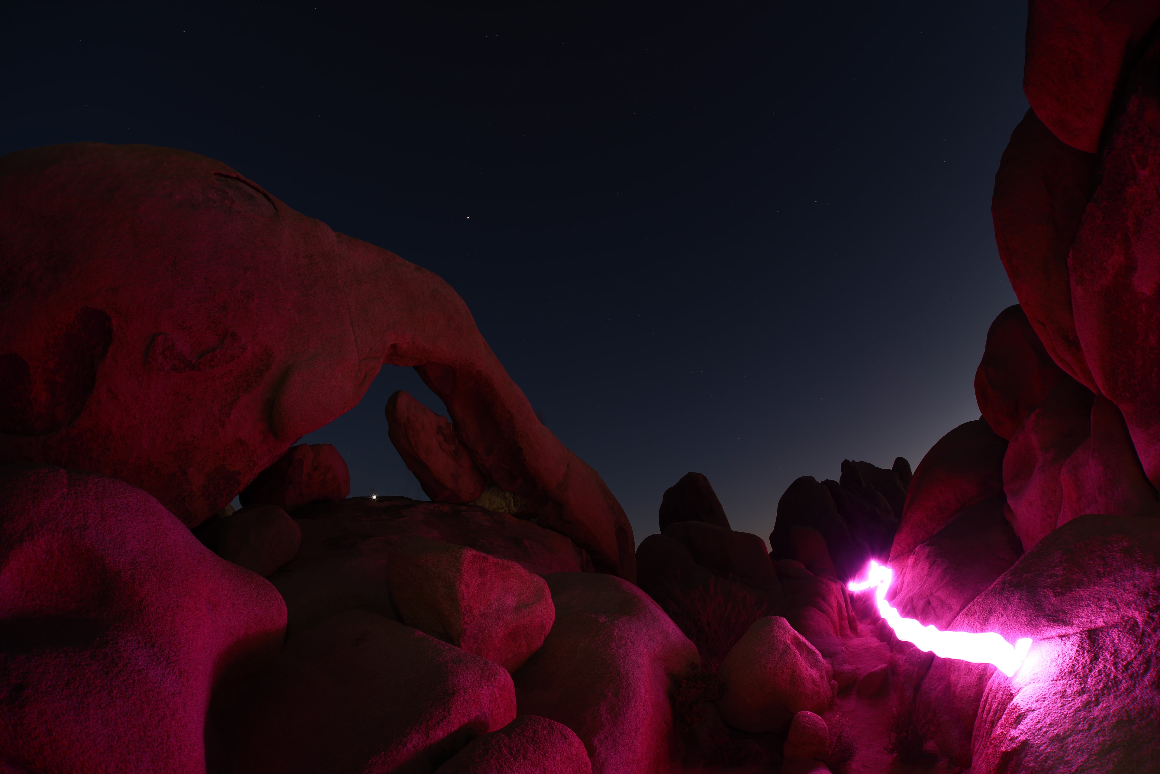 Desert rock formations illuminated in magenta light under a starry night sky