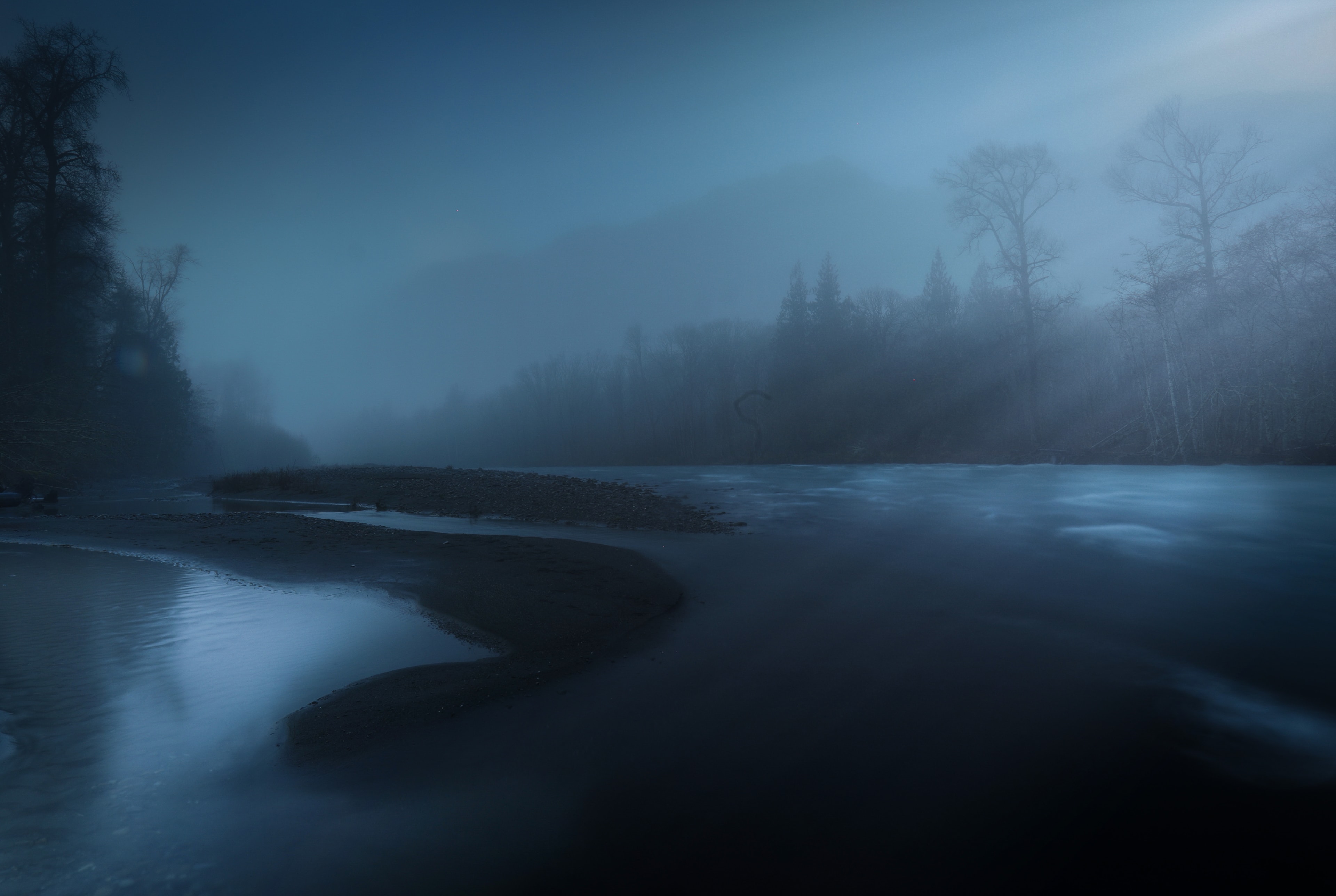 Misty blue river winding through foggy forest at dusk with silky long exposure water